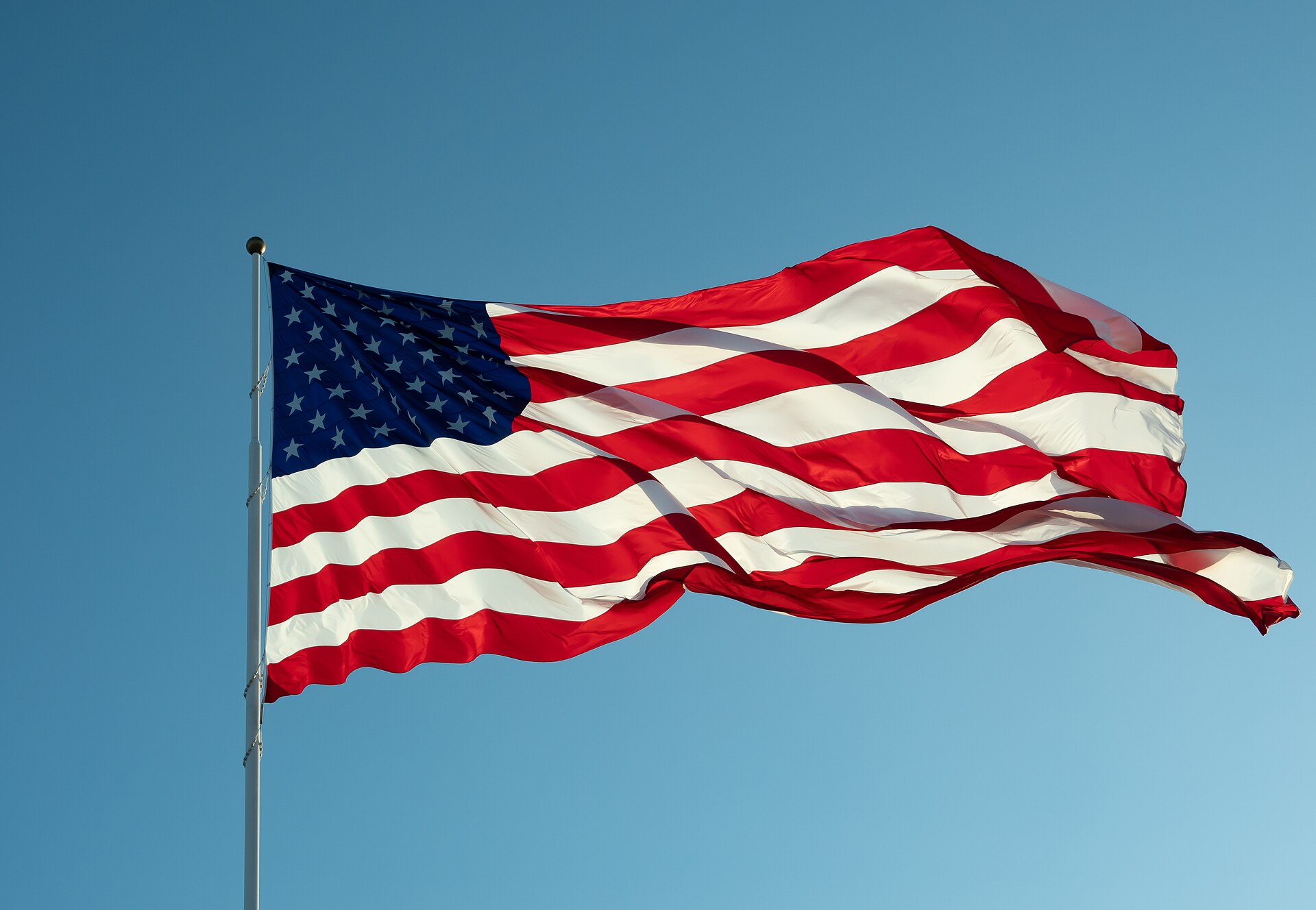 Fotografía de una gran bandera de Estados Unidos ondeando al viento bajo un cielo azul despejado